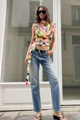 Jeans de tiro medio con corte slim fit, confeccionados en denim azul clásico. Presentan diseño de cinco bolsillos, cierre frontal con cremallera y botón, e incluyen un cinturón negro con hebilla metálica.