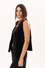 Chaleco oversize de cuero descarne color negro, con diseño de terminación en picos, flecos en la espalda y detalle de tachas metálicas a lo largo de los bordes frontales.