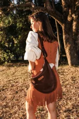 Chaleco entallado color marrón, confeccionado en cuero con detalles bordados en rojo y tachas metálicas. Presenta flecos de cuero en los laterales y un diseño de inspiración tribal.