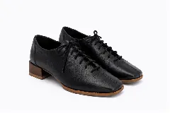 Zapatos acordonados de cuero color negro, con diseño de punta cuadrada, costuras centrales decorativas y suela marrón con taco bajo.