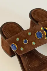 Sandalia de tacón ancho color marrón, confeccionada en gamuza, con puntera cuadrada, tira delantera fina y tira ancha superior decorada con apliques de piedras en tonos azules y bordes dorados.