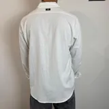Camisa de manga larga confeccionada en lino, color blanco, con cuello clásico y cierre frontal de botones.