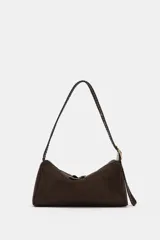 Bolso de hombro de diseño estructurado en color marrón, confeccionado en gamuza. Presenta un asa larga ajustable con detalle de trenzado y hebilla metálica dorada. Cuenta con cierre de cremallera con doble tirador y bolsillo interior.