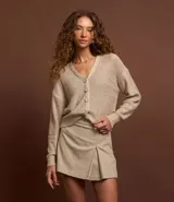 Cardigan color beige confeccionado en tejido de punto con lentejuelas, de corte regular, cuello en V, manga larga y cierre abotonado frontal.