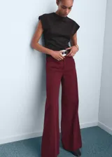 Pantalón de jean estilo wide leg, color bordó, con tiro alto, cinco bolsillos, cierre frontal con cremallera y botón, y trabillas para cinturón.