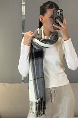 Bufanda rectangular de tejido suave con diseño de cuadros escoceses en tonos mostaza, blanco y gris, terminada con flecos en los extremos.