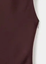Vestido largo de corte evasé en color marrón oscuro, con cuello alto y cierre de botones en la parte posterior. Presenta un diseño sin mangas con tirantes anchos y una costura diagonal en la cintura que aporta estructura a la prenda.