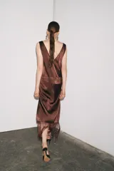 Vestido midi marrón con bordados florales y geométricos en el frente, escote redondo, mangas sisa, tejido plisado y flecos en el ruedo.