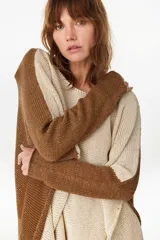 Poncho oversize de tejido de punto bicolor en tonos crudo y marrón, con hilos de lurex incorporados que aportan brillo. Presenta escote redondo amplio y aberturas laterales en el dobladillo.