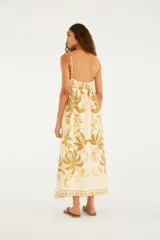 Vestido largo blanco de tirantes finos con estampado botánico en tonos mostaza y beige, escote en V profundo y falda amplia con vuelo.