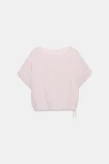 Camisa amplia de color rosado, con diseño estilo capa, cuello redondo y manga corta amplia. Cuenta con un bajo ajustable mediante lazada lateral.