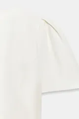 Top blanco de manga corta abullonada, con cuello redondo y cierre en la espalda con cremallera oculta.