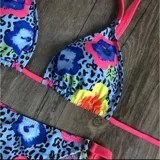 Conjunto de bikini United Uy modelo Mili, con estampado colorido de flores sobre fondo celeste con patrón de leopardo. El corpiño es de diseño triangular con tirantes fucsias y la bombacha es de corte tanga con detalles ajustables en los laterales.