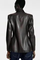 Blazer de corte cruzado confeccionado en material efecto piel, con cuello de solapa, manga larga con hombreras y cierre frontal con botones. Presenta bolsillos delanteros con solapa.