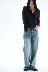 Cárdigan de punto color borgoña oscuro, con cuello redondo y manga larga. Presenta cierre frontal con botones dorados metálicos y remates acanalados en cuello, puños y bajo.