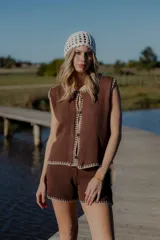 Conjunto de dos piezas tejido en algodón, compuesto por un chaleco sin mangas con cierre frontal de botones y un short de tiro medio. Ambas prendas presentan un diseño en color blanco con detalles de terminaciones en color beige.