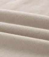 Remera de algodón color beige claro, manga corta y cuello redondo, con un pequeño estampado localizado en el pecho izquierdo de un escudo con una rosa de los vientos.