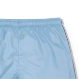 Short de baño Lacoste color celeste, con cintura elástica y cordón ajustable. Presenta bandas laterales con estampado de la marca y el logo del cocodrilo bordado en la pierna izquierda.