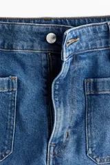 Jean de denim de algodón con leve stretch, tiro alto y pierna ancha de corte holgado. Cuenta con bolsillos de parche delanteros y traseros, y cierre de botón y cremallera.