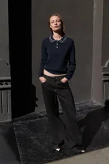 Jersey de punto color azul marino, de manga larga, con cuello polo y cierre frontal de botones. Presenta vivos blancos con borde ondulado en el cuello, puños y ruedo inferior.