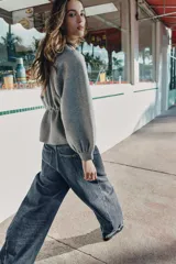 Jersey de punto color gris, con cuello redondo, mangas largas abullonadas con puños elásticos y cintura ajustable mediante cordón. Presenta una costura vertical marcada en la parte frontal.