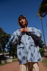 Campera de denim con estampado de lunares grandes en tono azul oscuro sobre fondo celeste. Presenta corte oversize, cierre frontal con botones metálicos y bolsillos frontales con solapa.