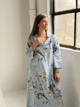 Vestido largo celeste con estampado floral en tonos blancos y grises, de corte holgado, mangas largas y cuello drapeado.