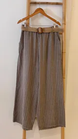 Pantalón marrón con rayas verticales blancas, corte palazzo y cintura alta con cinturón de rafia trenzada.