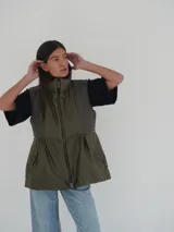 Chaleco verde seco con cuello alto, cierre frontal con cremallera y bolsillos laterales con cierre.