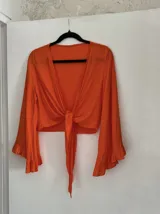 Blusa corta color naranja con escote en V, mangas largas acampanadas con volantes y nudo frontal.