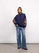 Buzo de algodón color negro con cuello redondo, mangas largas y bordado floral XL en color cobre en las mangas. Presenta un diseño holgado y cómodo.