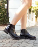 Botinetas de cuero negro con suela track dentada. Presentan un diseño de caña baja con paneles laterales elásticos y cierre lateral, combinando texturas de cuero liso y texturizado.