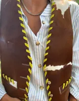 Chaleco de sastrería con estampado de manchas tipo cowhide, cierre frontal con botones y detalles de pasamanería en cuero rojo en los bordes y bolsillos. Presenta un diseño clásico con espalda en lino.