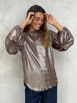 Blusa de manga larga con efecto metalizado o brillante, color marrón topo o bronce. Presenta cuello alto y mangas abullonadas con puños ajustados elásticos. El ruedo inferior es ondulado.