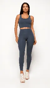 Conjunto deportivo de dos piezas en color gris oscuro, compuesto por un top de tirantes anchos con escote redondo y largo extendido con recortes en la cintura, y una calza de tiro alto con costuras modeladoras.