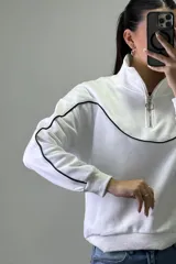 Buzo deportivo color beige con cuello alto y cierre frontal parcial. Presenta costuras decorativas con ribetes blancos en el pecho y a lo largo de las mangas. Posee puños y ruedo elásticos.