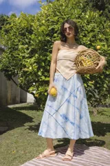 Falda midi evasé de algodón, teñida artesanalmente con índigo, creando un patrón de rayas y bloques en tonos blanco y azul. Presenta una construcción con recortes diagonales y cintura elastizada.