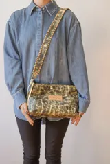 Cartera tipo sobre o neceser de cuero uruguayo, forrada en tela panamá. Presenta un acabado pintado con efecto desgastado en tonos dorado y negro/verde oliva. Incluye correa removible.