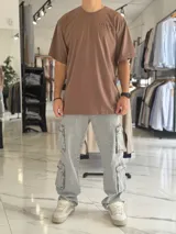 Remera oversize color beige, con diseño estampado en la espalda que incluye tipografía grande y texto descriptivo en negro.