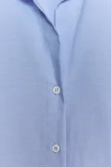 Camisa básica de algodón con cuello solapa, escote en pico y cierre frontal con botones. Presenta mangas largas con puños abotonados y bajo redondeado.