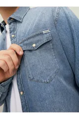 Camisa de denim celeste de manga larga, con cuello clásico, cierre frontal con botones a presión y dos bolsillos con solapa abotonada en el pecho.