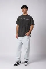 Remera de algodón peinado con efecto desgastado (snow wash), color gris oscuro. Presenta un estampado frontal con texto y un patrón de cuadros de carreras.