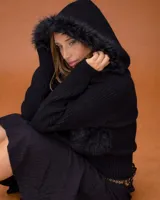 Campera de diseño combinado con cuerpo en textura de piel sintética y mangas tejidas. Presenta una capucha amplia con borde de pelo sintético y cierre frontal.