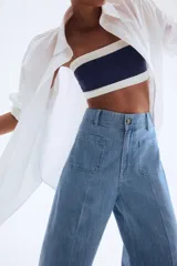 Pantalón de jean de denim rígido, color celeste claro, tiro alto, pierna amplia y corte holgado. Presenta pliegues frontales y traseros, cierre con botón y bolsillos parche en la parte delantera y trasera.