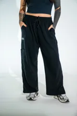 Pantalón de corte holgado y estilo urbano, color negro, con cintura elástica ajustable mediante cordón y bolsillos laterales. Presenta un pequeño estampado en la pierna derecha.