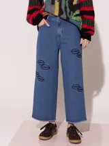 Pantalón de jean azul de corte ancho, tiro medio alto y largo a la altura del tobillo. Presenta apliques bordados con forma de labios.