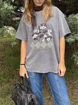 Remera de algodón gris con efecto lavado, de corte holgado y manga corta. Presenta un estampado frontal con diseño de árboles y figuras geométricas a cuadros, acompañado por la frase 'Jardín de Invierno'.