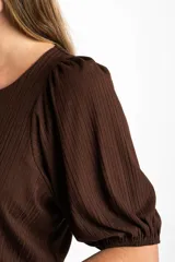 Remera de color marrón con textura acanalada, cuello redondo y mangas cortas abullonadas con terminación elástica.