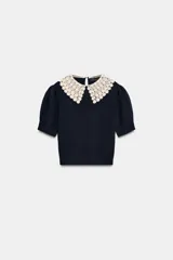 Jersey de punto color azul marino, con cuello de solapa en crochet color crema y manga corta abullonada. Cierre en la espalda con abertura y botón de perla.