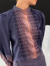 Chaqueta entallada de algodón tipo seda, teñida a mano con técnica tie-dye en tonos azul y naranja. Tiene cuello mao, mangas largas con puños abullonados y cierre frontal con broches.